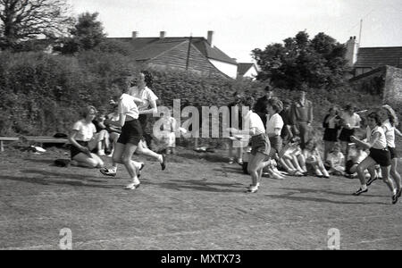 1960, historical picture of secondary schoolgirls taking part in relay race at a inter-school county sports day, Dorset, England, UK. The girl athletes are running up to their teammates to pass them the batons for the next leg of the race. Stock Photo