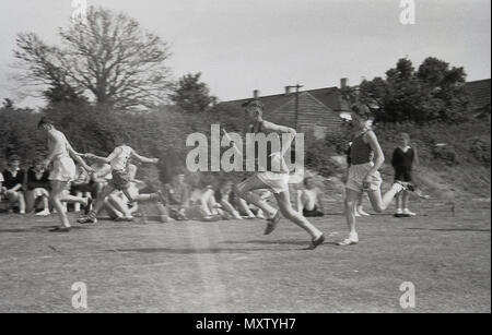1960, historical picture, secondary schoolboys taking part in an inter-school county sports day, Dorset, England, UK. Here we see them competing in a team relay race on a grass track, as the runners pass the baton to their teammate for the next leg of the race. Stock Photo