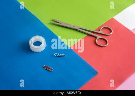 On colorful sheets of paper are scissors, paper clips, tape. Stock Photo
