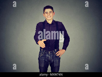 Smiling stylish young man outstretching hand at camera to give greeting handshake on gray Stock Photo