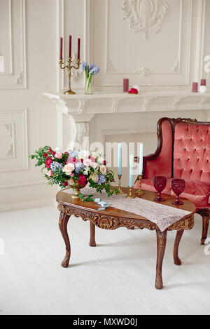 Decorated vintage table in white baroque style interior with red luxury sofa. Table is set for romantic event. Stock Photo