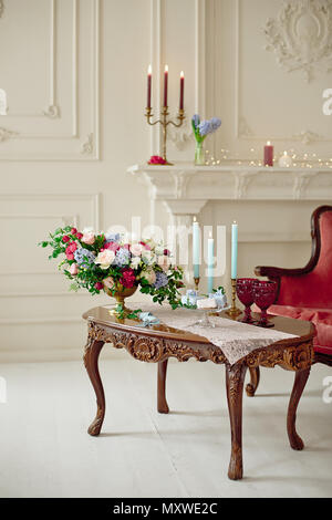 Decorated vintage table in white baroque style interior with red luxury sofa. Table is set for romantic event. Stock Photo