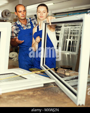Positive man and woman in blue overalls assembling pvc windows at factory Stock Photo