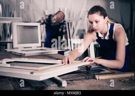 Workwoman is checking dimensions of finished plastic window using measuring tape at factory. Stock Photo