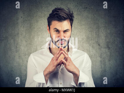 Young man holding hands together and looking at camera with thoughts of revenge and jealousy Stock Photo