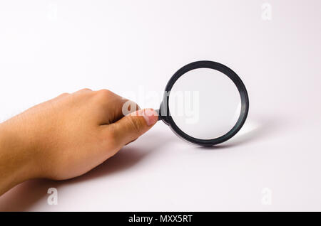 A hand is holding a magnifying glass against a white background. Find information and things, special search capabilities. High level of service, exce Stock Photo