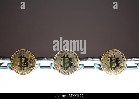 Three Bitcoins sits on a white glowing surface while a heavy steel metal chain sits behind.  Concepts of block chain technology and digital currency. Stock Photo