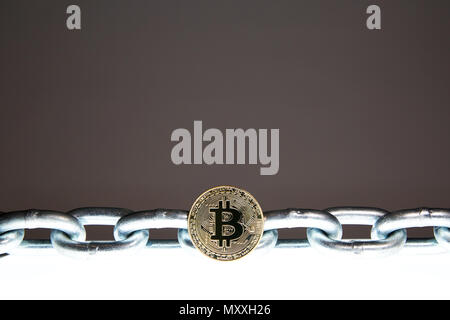 A Bitcoin sits on a white glowing surface while a heavy steel metal chain sits behind.  Concepts of block chain technology and digital currency. Stock Photo