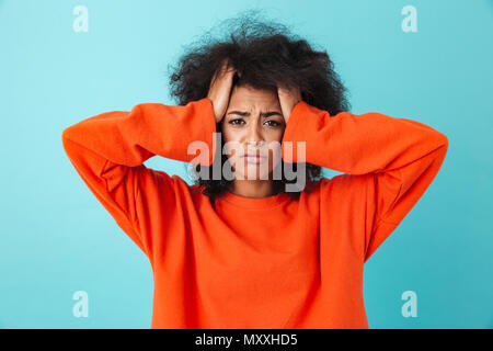 Image closeup of frustrated woman in red shirt looking on camera and grabbing head with shaggy hair isolated over blue background Stock Photo