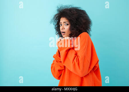 Colorful image closeup of scared woman in red shirt posing on camera and pressing arms to chest in fear isolated over blue background Stock Photo