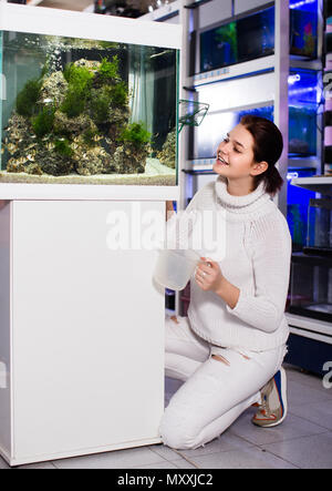 happy italian girl holding aquarian net and water container next to aquarium with colorful fish in aquarium shop Stock Photo