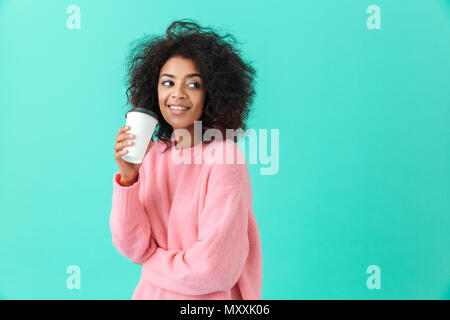 Portrait of american woman 20s with afro hairdo looking aside while drinking takeaway coffee or tea from paper cup isolated over blue background Stock Photo