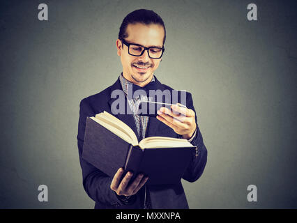 Young man in suit and glasses scanning information in book using phone and breaking copyrights. Stock Photo