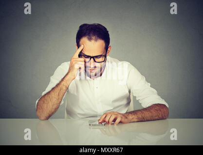 Man in glasses concentrating on smartphone remembering password while sitting at table in puzzlement Stock Photo