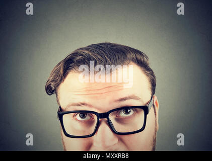 Closeup of chunky man in eyeglasses looking up and having question to ask on gray background Stock Photo