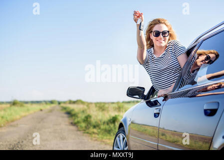 An attractive woman in a car holds a car key in her hand. Stock Photo