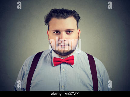 Young bearded chubby man wearing formal outfit with red bow tie looking  contently at camera on gray Stock Photo - Alamy