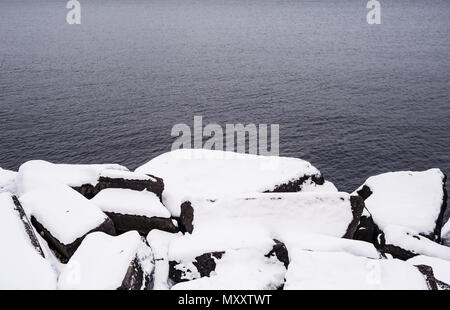 Pile of boulders covered in snow at lake in winter. Stock Photo