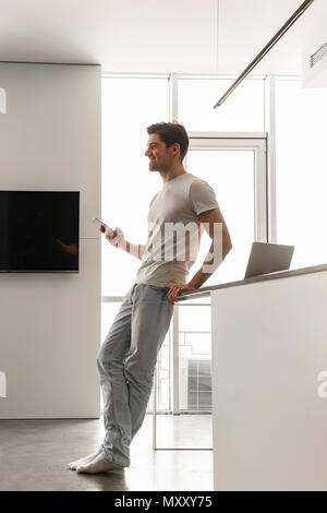 Full length photo in profile of handsome man in basic clothing using mobile phone while staying at home Stock Photo