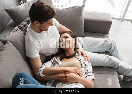 Photo of loving husband and wife in casual clothing resting in living room in modern flat and lying on sofa together Stock Photo