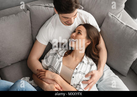 Photo of happy atractive man and woman smiling and hugging while resting together in apartment Stock Photo