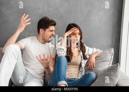 Photo of disappointed couple sitting together on sofa at home while man shouting on woman with blame isolated over white background Stock Photo