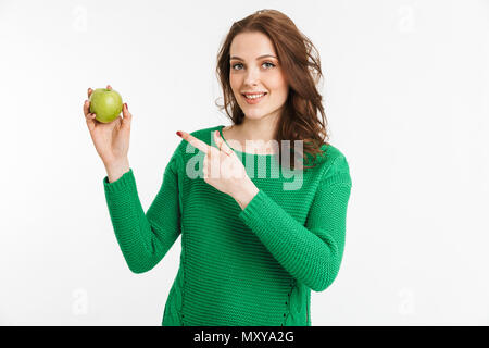 Portrait of a smiling young woman pointing finger at green apple isolated over white background Stock Photo