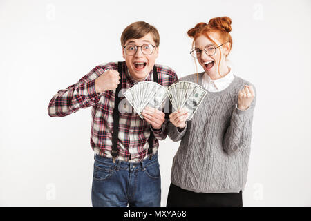 Excited couple of school nerds holding bunch of money banknotes and celebrating isolated over white background Stock Photo