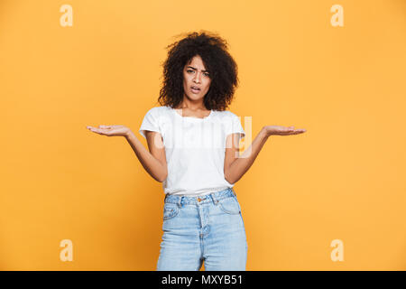 Portrait of a confused young african girl holding copy space isolated over yellow background Stock Photo