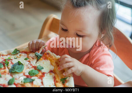 One Year boy sits in director chair in a public cafe indoor and eating italian pizza, children's fast food Stock Photo