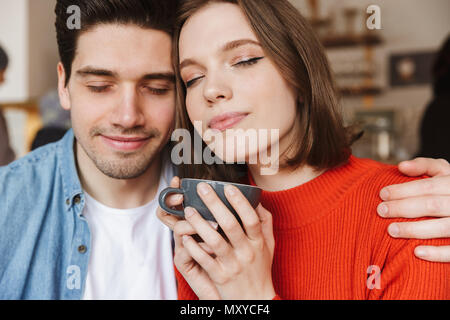 Happy couple woman and man taking pleasure with closed eyes while resting in restaurant and drinking coffee or tea together Stock Photo