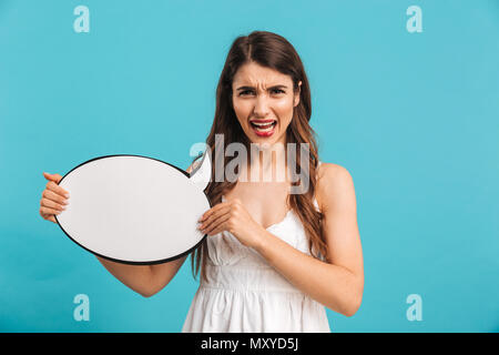 Portrait of a mad young girl in summer dress showing empty speech bubble isolated over blue background Stock Photo