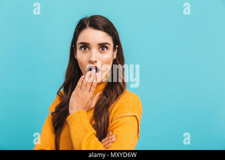 Portrait of a shocked miling young girl in sweater covering mouth with hand isolated over blue background Stock Photo