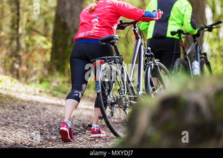 two unrecognizable persons hike with bicycle in the forest Stock Photo