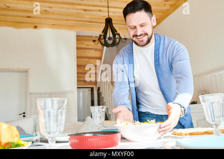 Portrait of mature bearded man setting table and smiling happily while waiting for guests at dinner in sunlit dining room at home, copy space Stock Photo