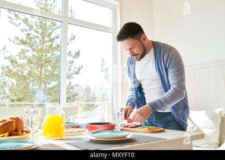 Side view portrait of mature bearded man setting dinner table  while waiting for guests  in sunlit dining room at home, copy space Stock Photo