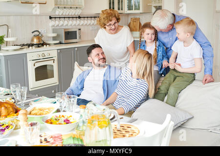 Portrait of happy two generation family enjoying dinner party together in modern apartment standing round couch with two adorable children in sunlight Stock Photo