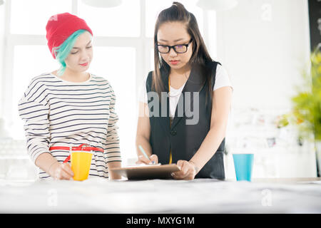Portrait of two contemporary young women making patterns for clothes on tailors table while collaborating  on creative fashion design project in small Stock Photo
