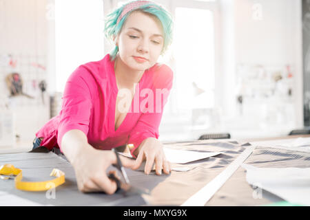 Portrait of cheerful young woman with mint hair working at tailors table creating fashion design project in modern atelier studio, copy space Stock Photo