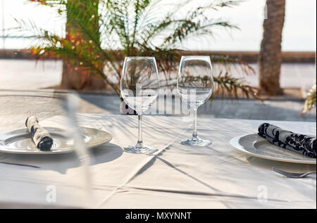 Table setting with a wine glasses, cutlery and plates. Outdoors restaurant. Tropical landscape