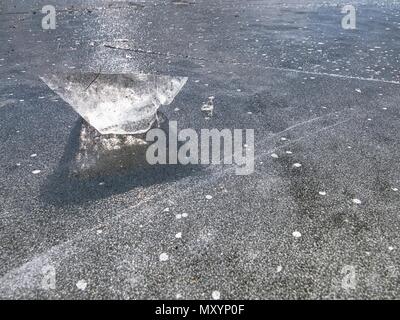 Charming winter sun hiden behind pice of clear ice. Shining piece of ice lies on lake ice and create beautiful reflection. Stock Photo