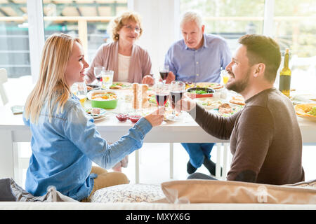 Portrait of happy modern couple clinking wine glasses during family dinner in sunlight Stock Photo