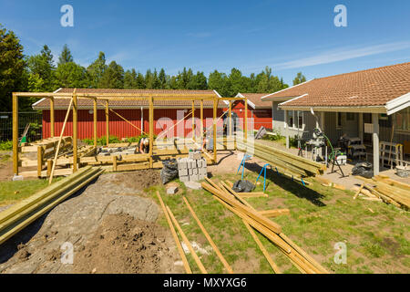 Joiners working outdoors on erecting a large patio with pergola and round firepit Stock Photo