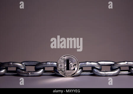 A LiteCoin sits on a white surface while a heavy steel metal chain sits behind.  Concepts of block chain technology and digital currency. Stock Photo