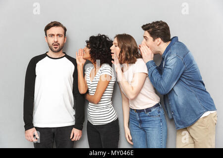 Image of group of friends standing isolated over grey wall background gossiping tell secrets talking with each other. Stock Photo