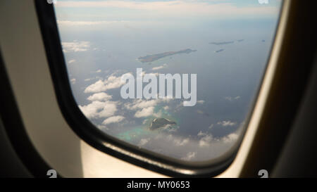 View through an airplane window on the tropical island, ocean, sky and clouds. Aerial view sea, clouds and sky as seen through window of an aircraft. Travel concept. Stock Photo