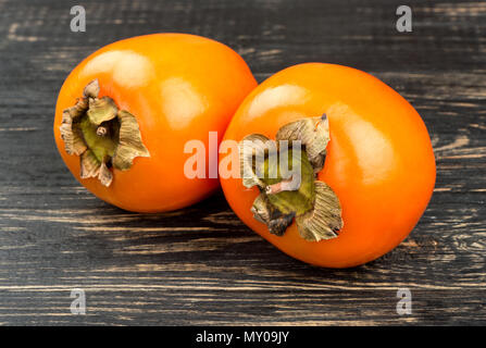 Fruit two ripe persimmons on wooden background closeup