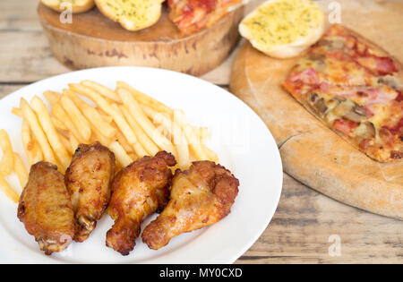 Fast food, crispy chicken wings,bread,french fries and pizza on wood background. Stock Photo