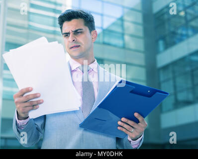 Businessman holding folder with documents and attentively reading Stock Photo
