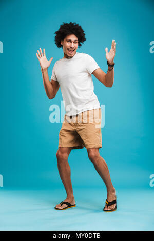 Image of excited emotional young african curly man standing isolated over blue background looking camera. Stock Photo